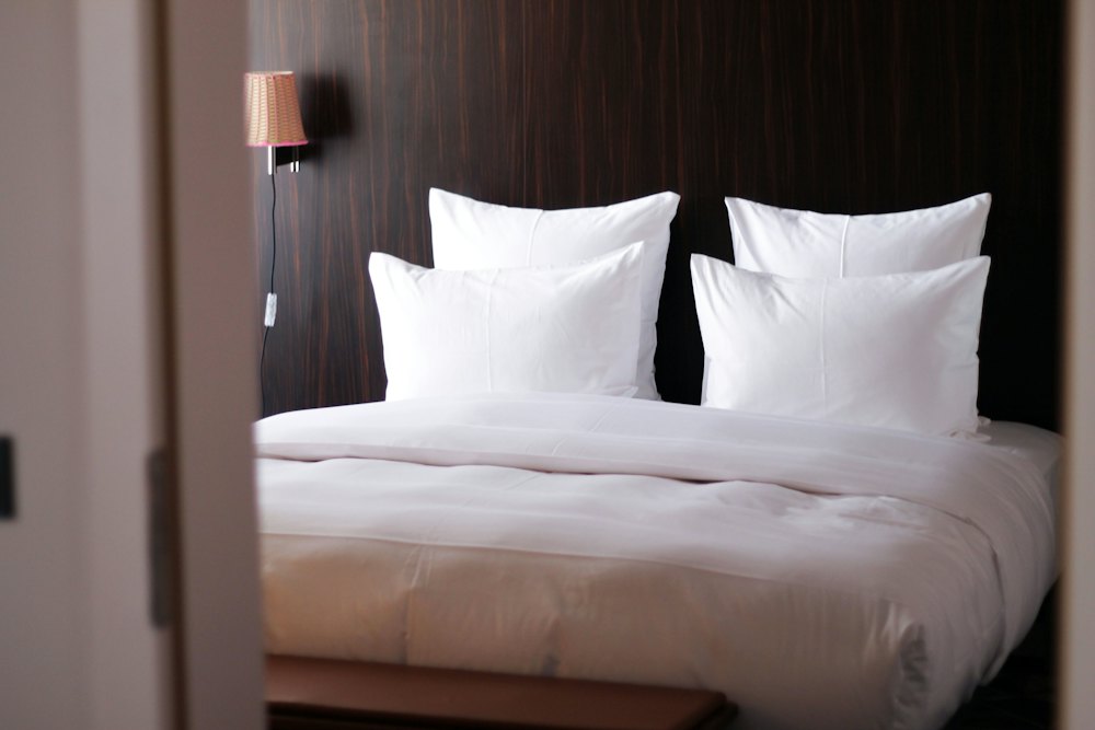 A king bed made up with white linen against a dark wood wall