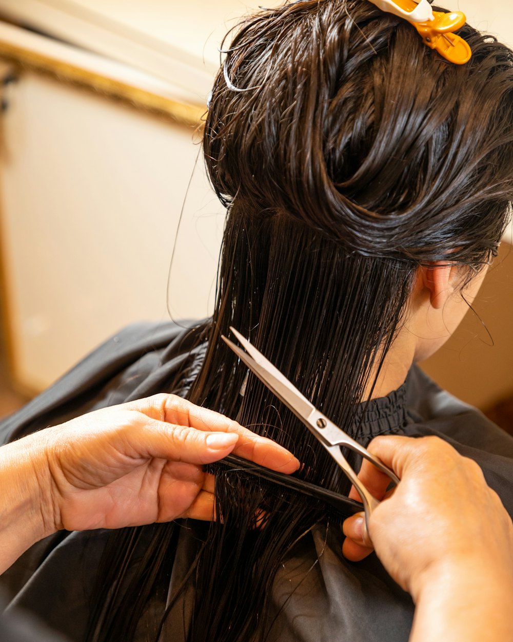 A stylist trimming dark hair with scissors