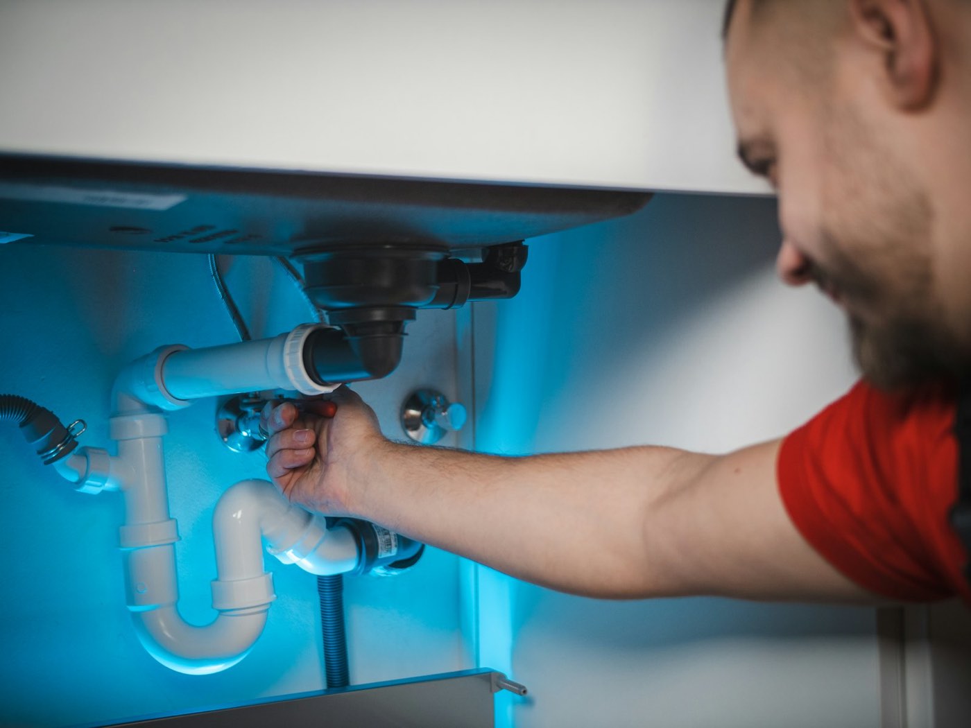 A plumber fitting a waste pipe under a basin
